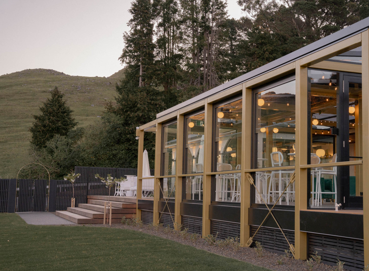 A contemporary, glass-fronted event space at The Hilltop in Christchurch, featuring an illuminated interior and outdoor patio.