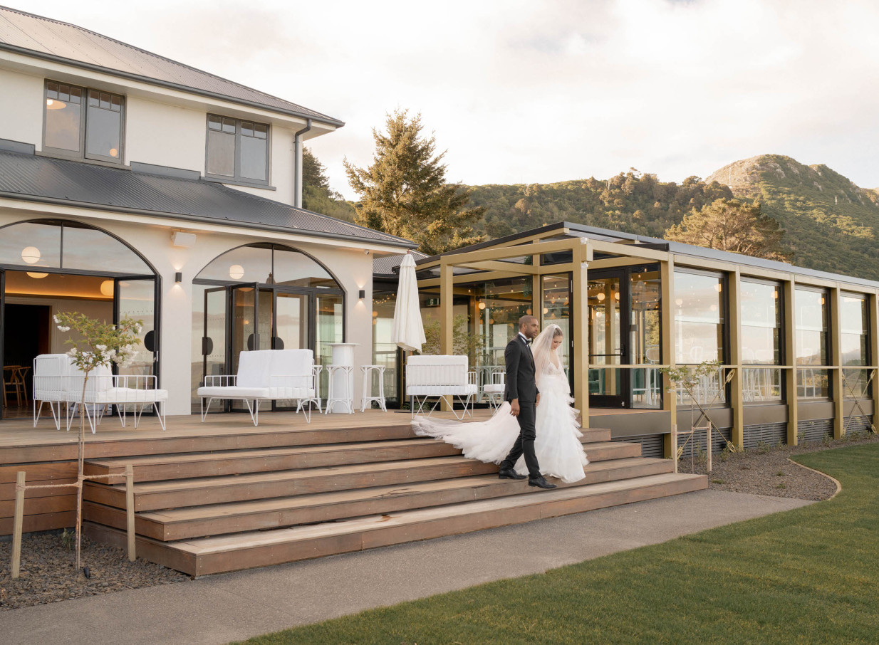 A newlywed couple strolls on the sleek, contemporary outdoor deck at The Hilltop, a modern wedding venue in Christchurch.