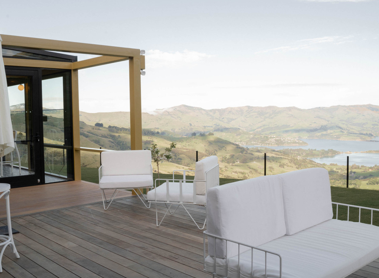 The modern outdoor lounge deck at The Hilltop, Christchurch, boasts panoramic harbour views over green hills.