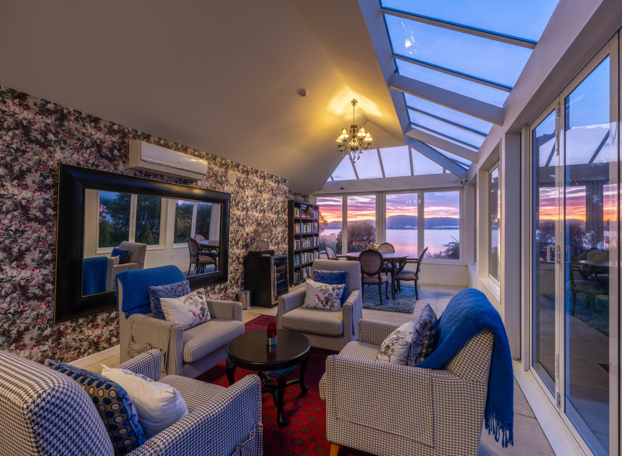 The luxurious conservatory lounge of the Black Swan Lakeside Boutique Hotel, Rotorua, overlooks the lake at sunset.
