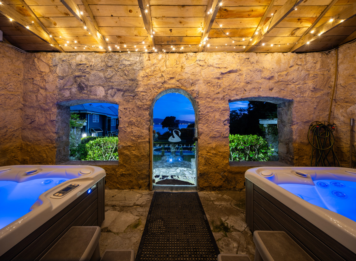 The secret grotto spa with dual hot tubs, featuring rustic stone walls and a lake view, at Black Swan Lakeside Boutique Hotel, Rotorua.