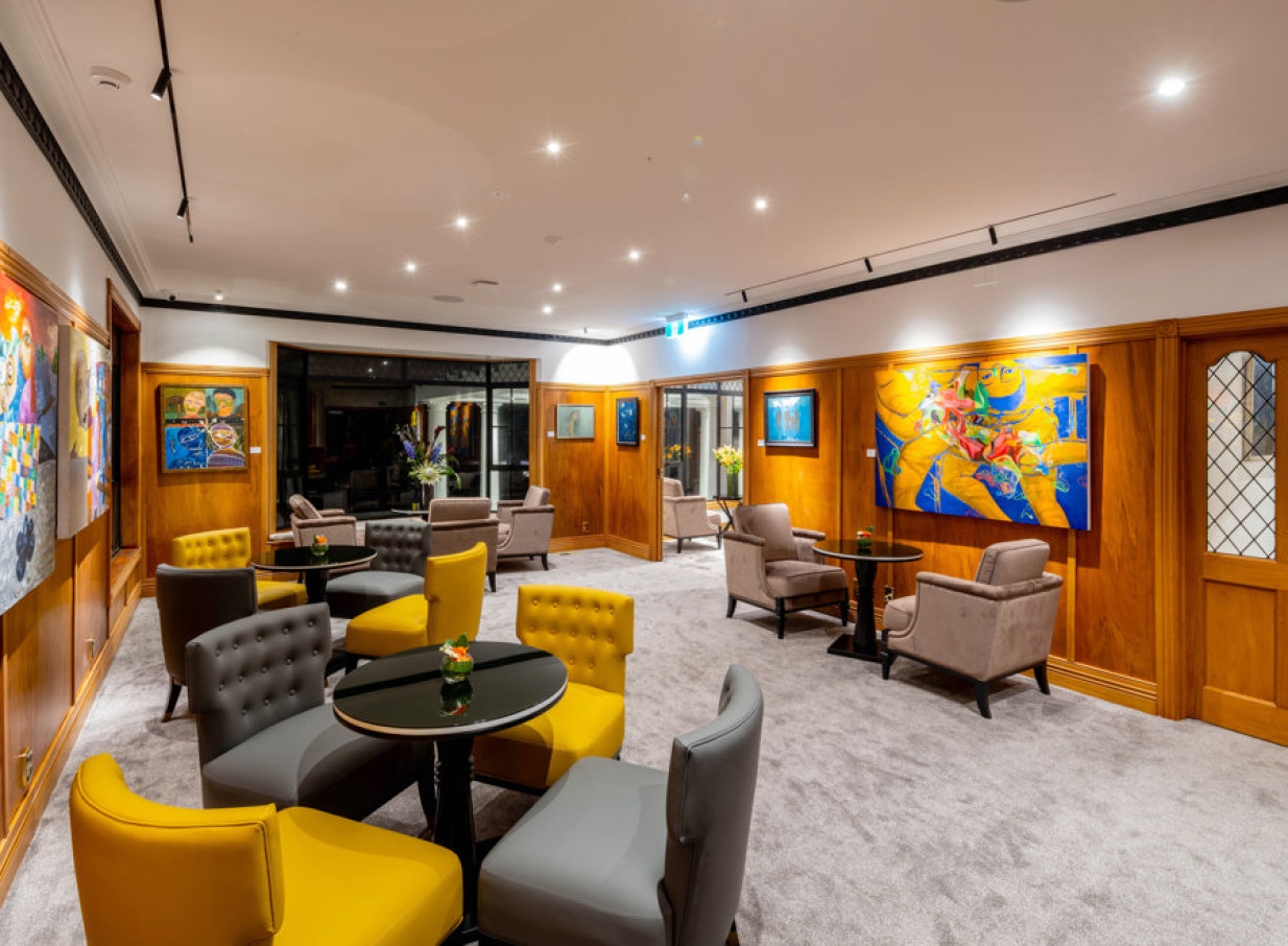 An elegant, art-filled lounge with modern grey and yellow seating and warm wood paneling at Hana Lodge, Rotorua.
