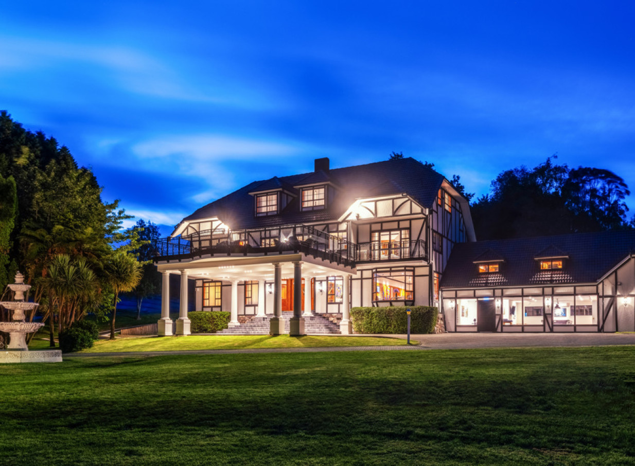 The elegant country lodge exterior of Hana Lodge in Rotorua glows at night amidst its sprawling grounds.