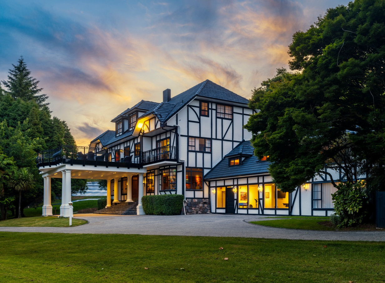 The elegant Tudor-style exterior of Hana Lodge in Rotorua is beautifully illuminated at dusk.