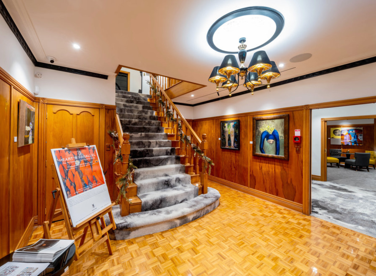 The elegant entrance hall of Hana Lodge in Rotorua features a grand carpeted staircase, warm wood paneling, and curated artworks.