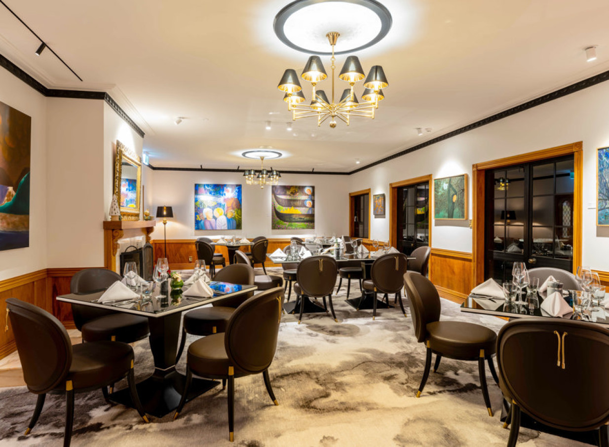 The elegant dining room at Hana Lodge, Rotorua, combines modern art, ornate chandeliers, and classic wooden accents for a refined atmosphere.