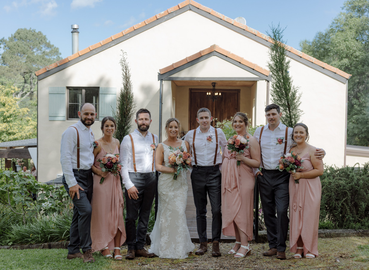 A wedding party stands before Villa Vie, a French country farmhouse-style venue in Bay of Plenty.