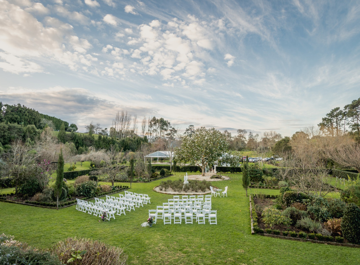 Elegant outdoor ceremony setup with white chairs in the manicured gardens of Villa Vie, a French-style estate in Bay of Plenty.