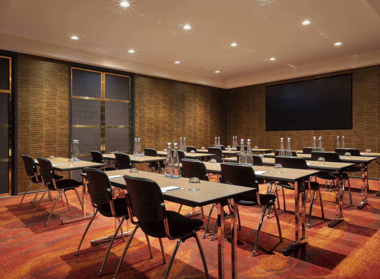 A modern, classroom-style meeting room with textured gold walls and a large screen at SO/ Auckland, Auckland.