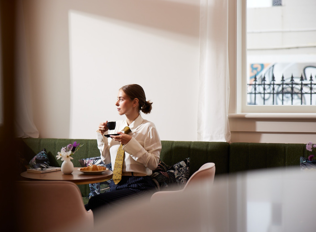 Woman enjoys coffee and a croissant in the timelessly elegant cafe of The Clements Hotel, Waikato.