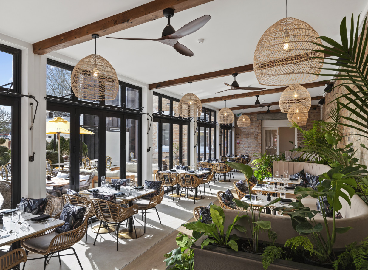 The Clements Hotel in Waikato offers a bright, contemporary dining room with natural light, rattan accents, and abundant greenery.