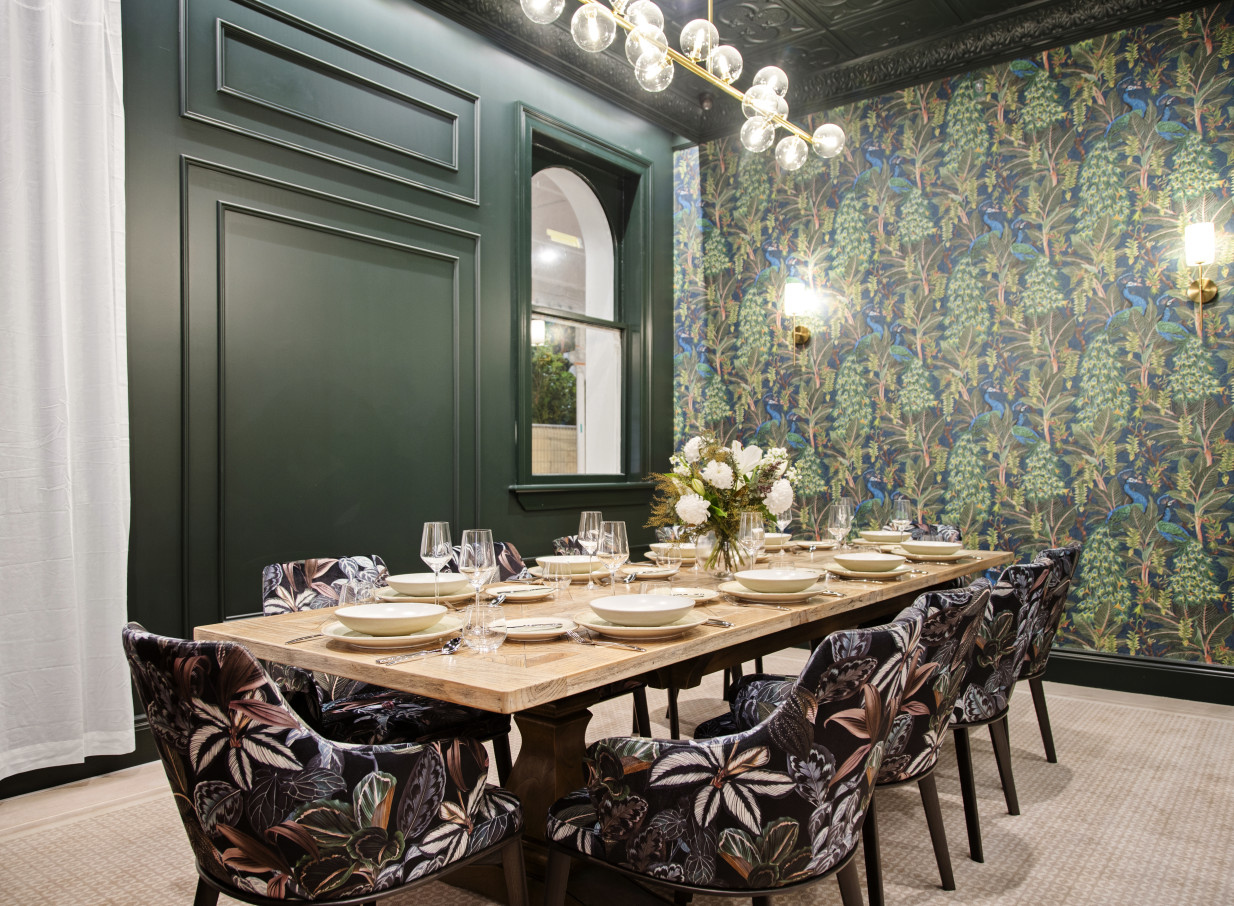 A private dining room at The Clements Hotel, Waikato, features elegant place settings, dark green paneling, and vibrant, patterned wallpaper.