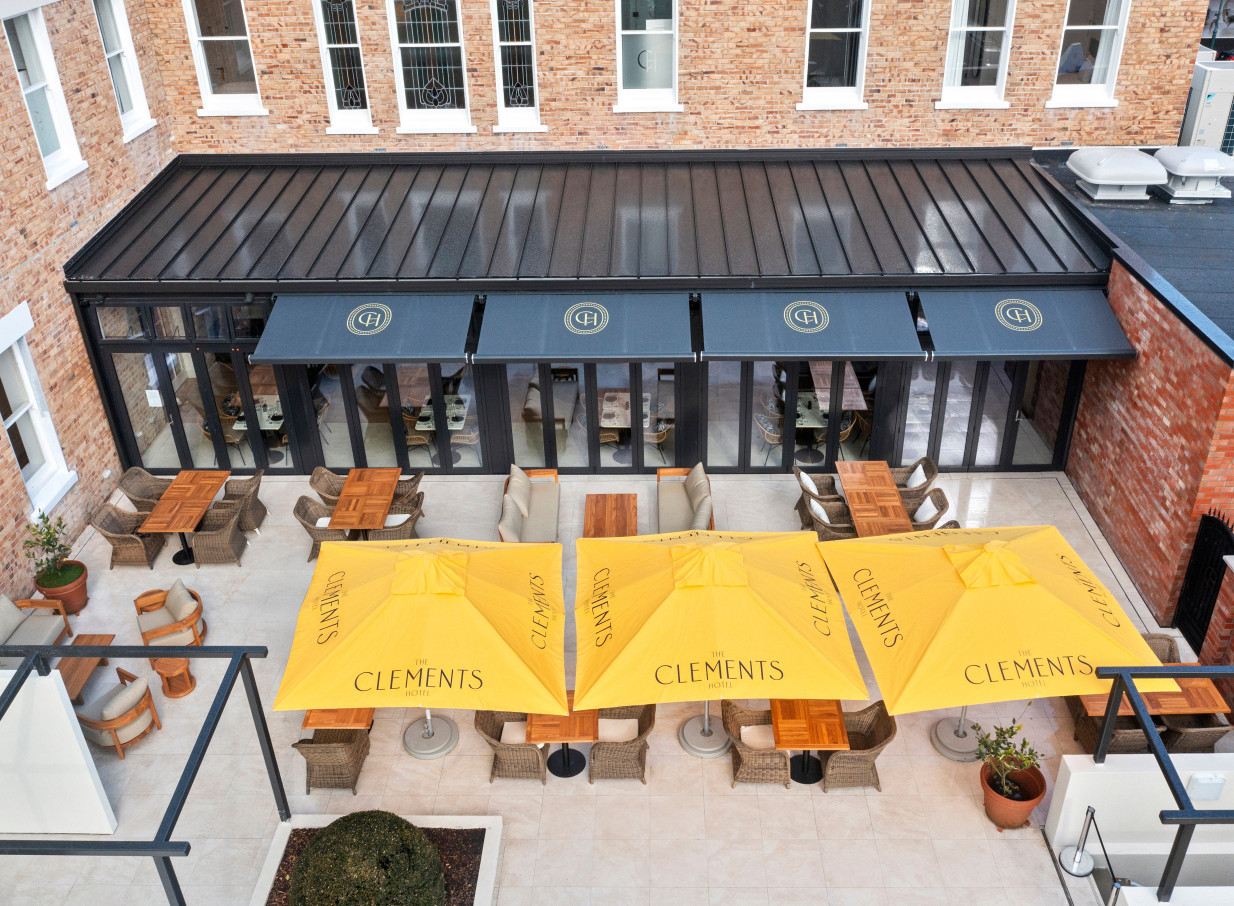 An outdoor dining terrace at The Clements Hotel in Waikato, showcasing its elegant Beaux Arts architecture with modern furnishings.
