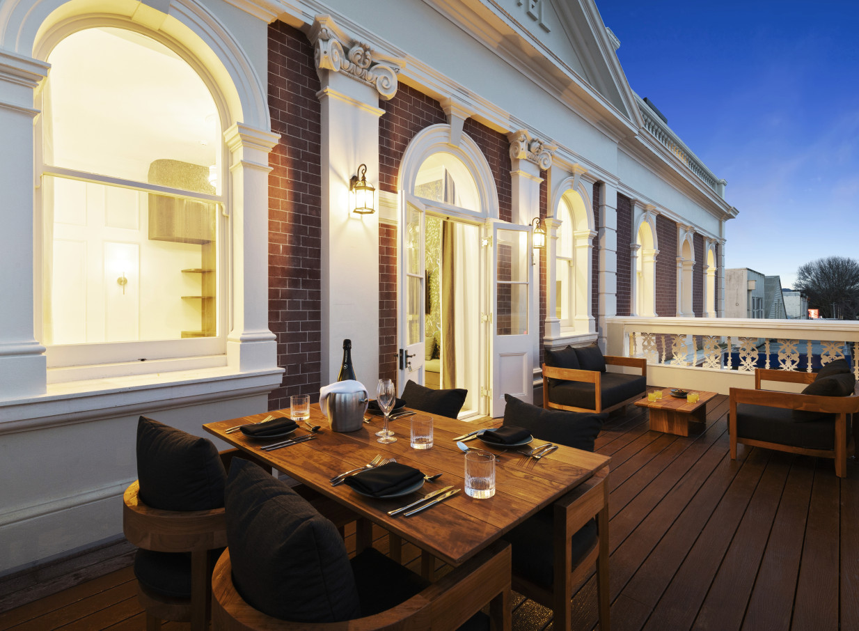 An elegant Beaux-Arts style balcony with outdoor dining and lounge seating at The Clements Hotel in Waikato.