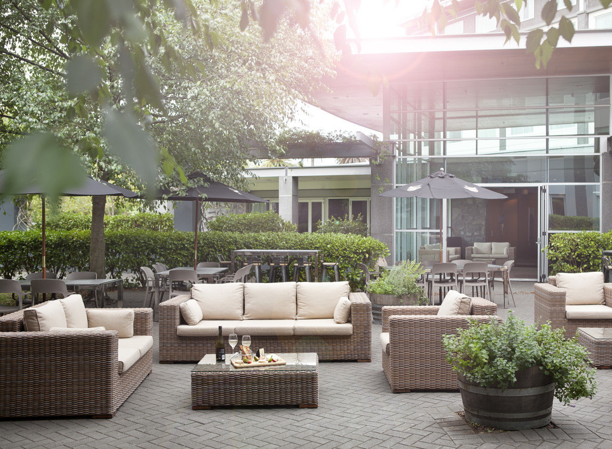 Novotel Auckland Ellerslie's modern outdoor lounge patio offers comfortable wicker seating amidst lush garden surroundings.