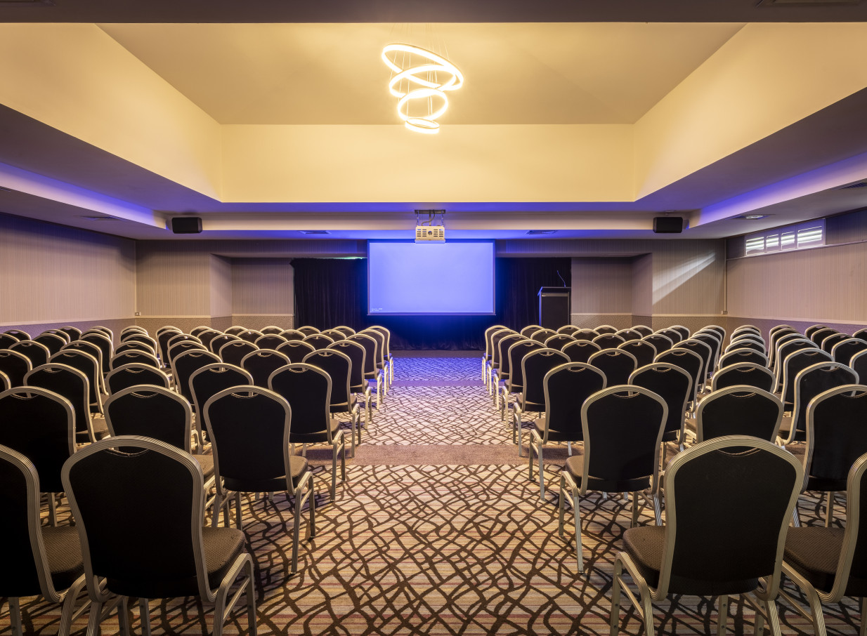 Modern theatre-style conference room at Waipuna Hotel & Conference Centre, Auckland, featuring a projector screen and stylish lighting.