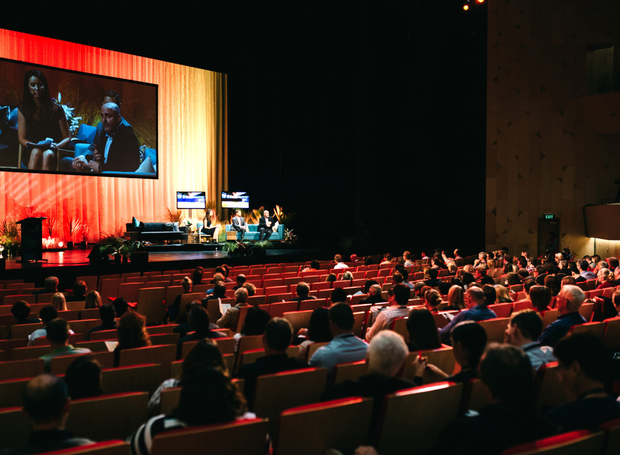A panel discussion unfolds in a modern theatre at Aotea Centre, Auckland, under vibrant lighting.