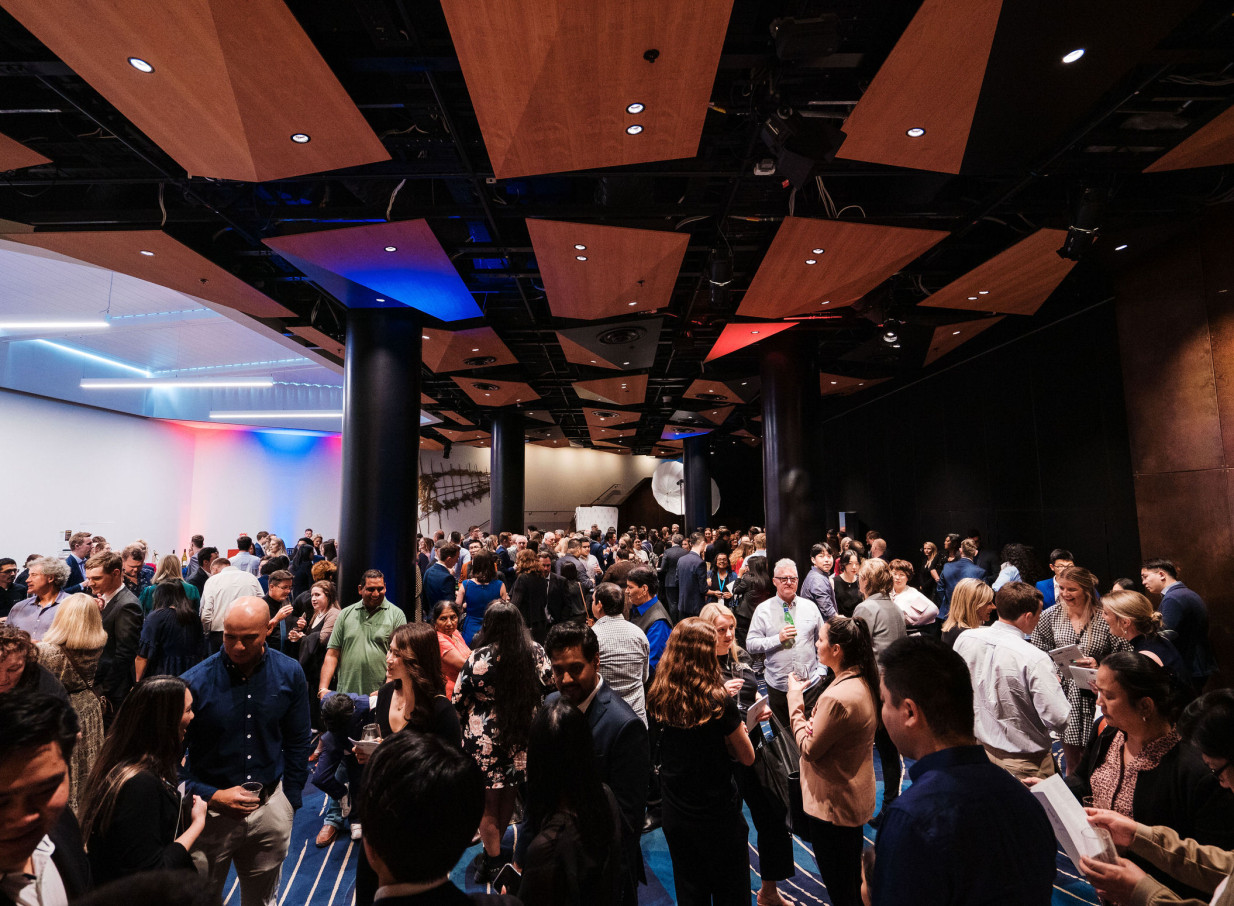A large, modern event space at Auckland's Aotea Centre, featuring angular timber ceiling panels and linear lighting, is bustling with a cocktail reception.