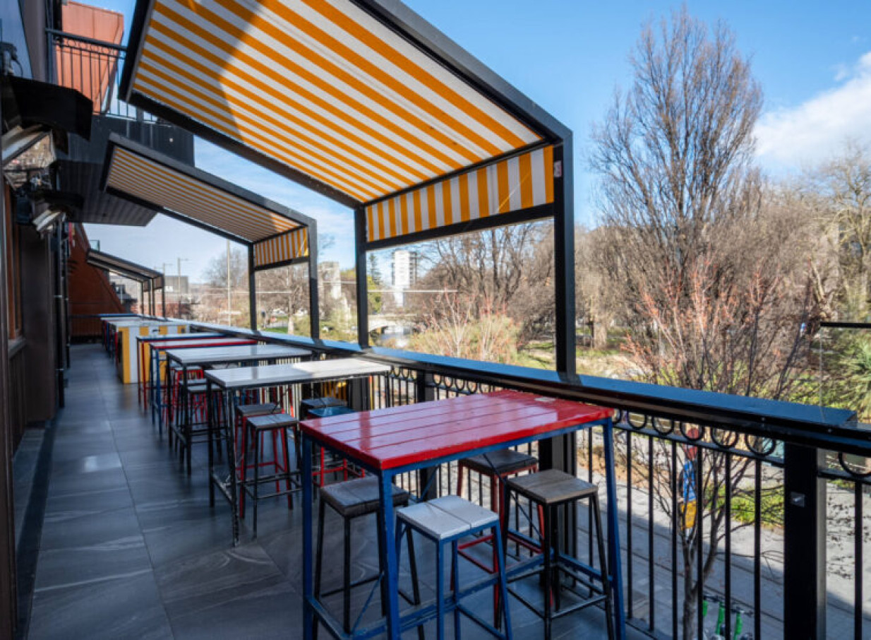 Fat Eddie's vibrant Christchurch balcony bar offers colorful seating, striped awnings, and scenic views.