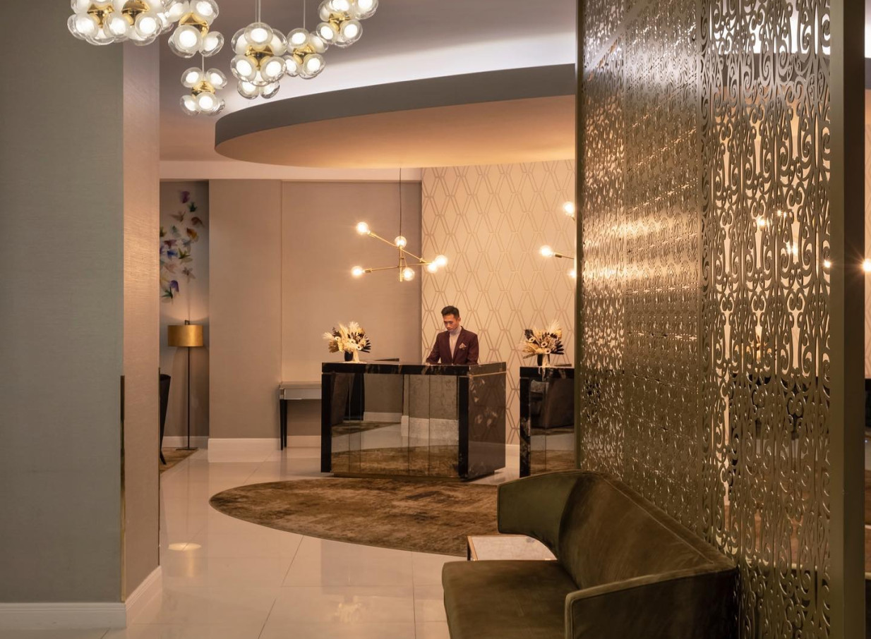 The modern and elegant lobby reception of Mövenpick Hotel Auckland features a staff member at the chic desk, with a striking decorative screen.