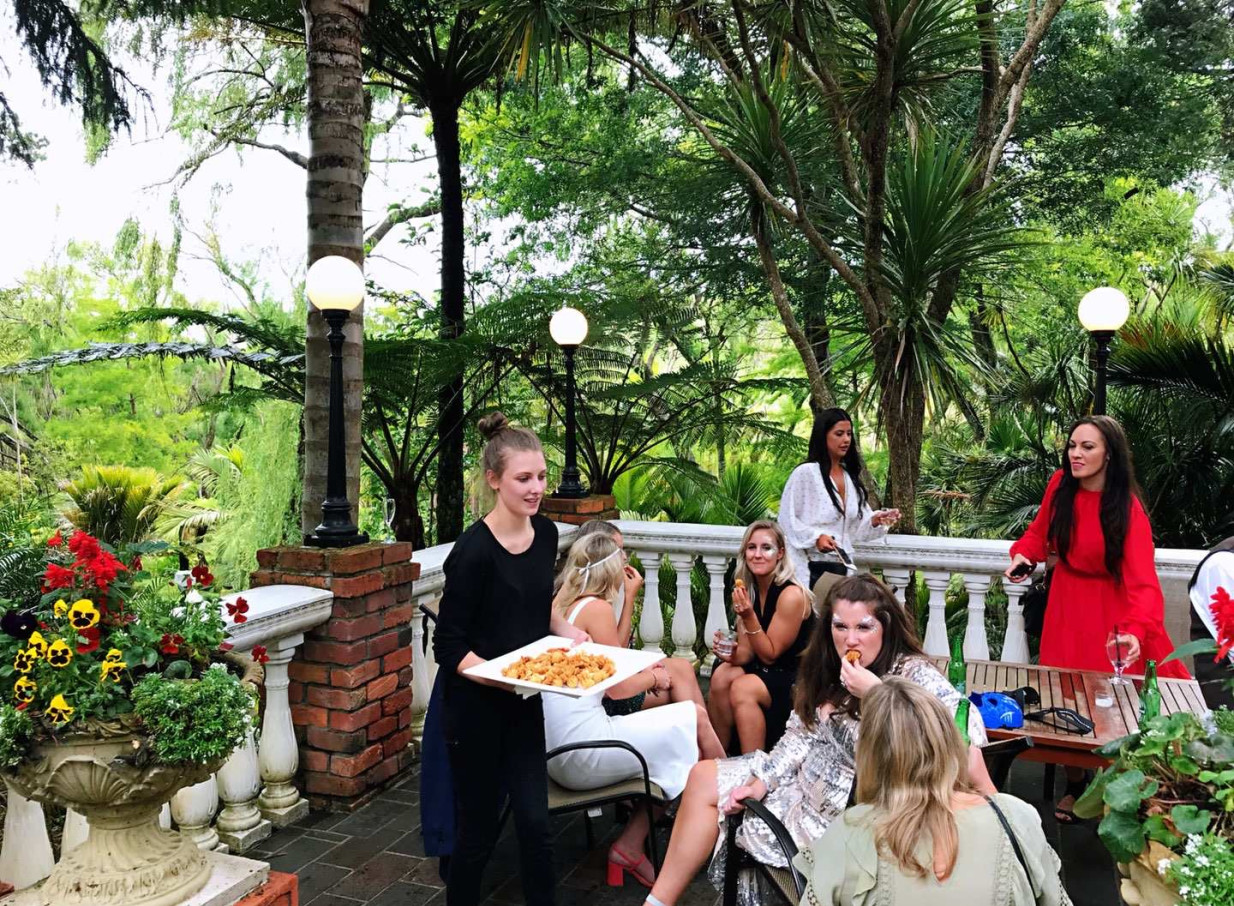 An outdoor reception at the historic Settlers Country Manor in Auckland, featuring guests enjoying canapés amidst lush, landscaped gardens.
