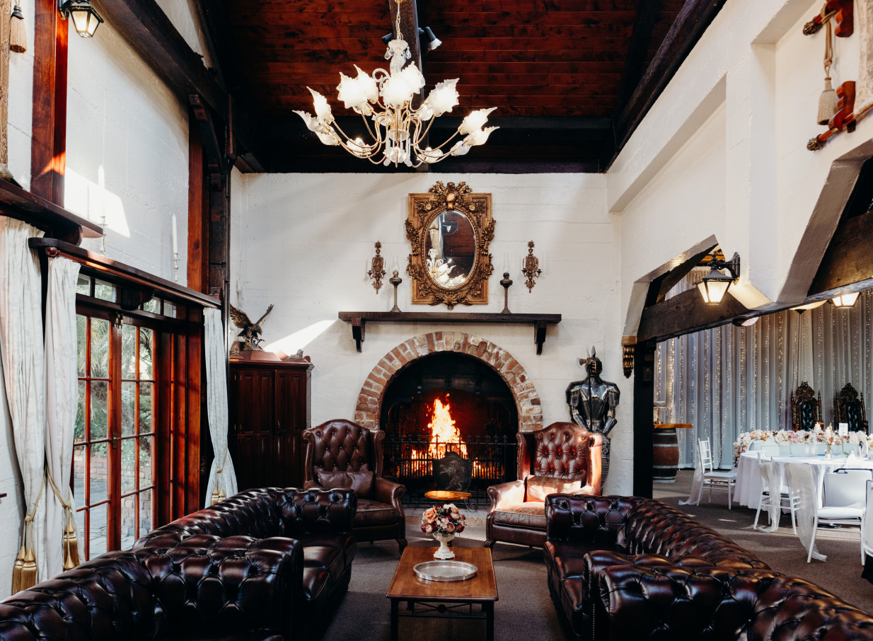 A charming heritage lounge at Settlers Country Manor in Auckland, featuring a brick fireplace and classic leather seating.
