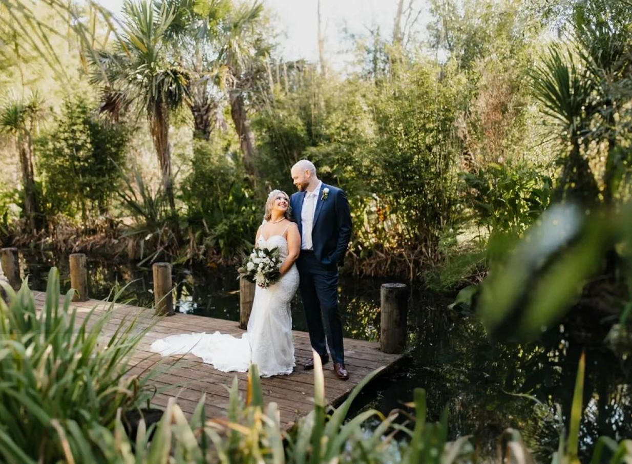 A couple poses on a wooden jetty amidst the lush, heritage gardens and waterways of Settlers Country Manor in Auckland.