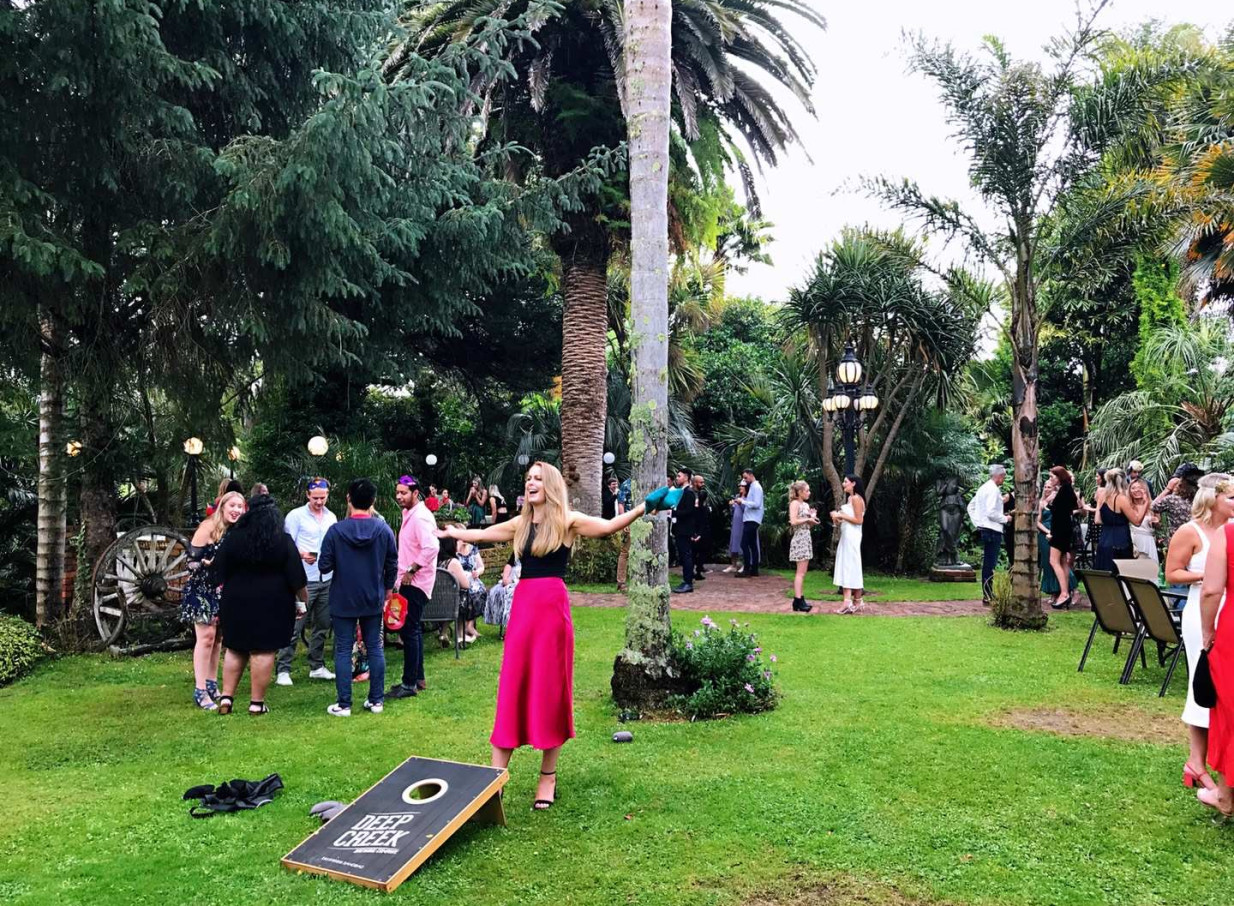 Guests mingle and play cornhole on the verdant lawn of Settlers Country Manor, a heritage estate with stunning gardens in Auckland.