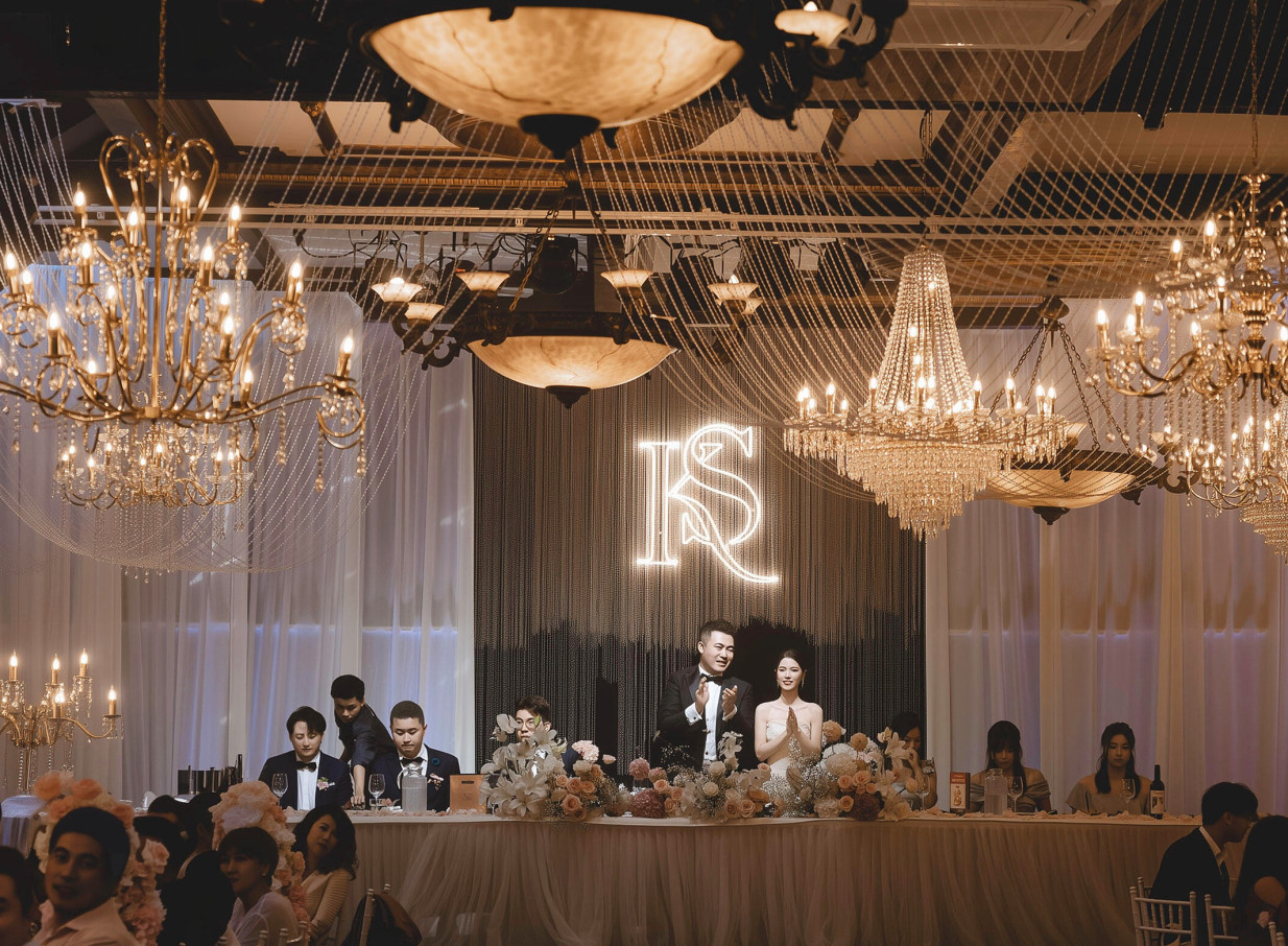An elegant indoor wedding reception with ornate chandeliers and a glowing neon sign at the heritage-style Settlers Country Manor in Auckland.