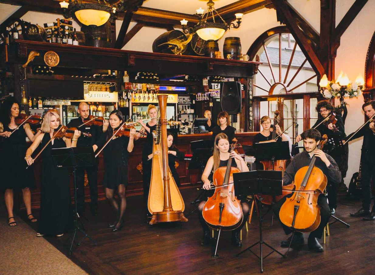 An orchestra performs in the rustic, timber-beamed interior of Settlers Country Manor, a heritage venue in Auckland.