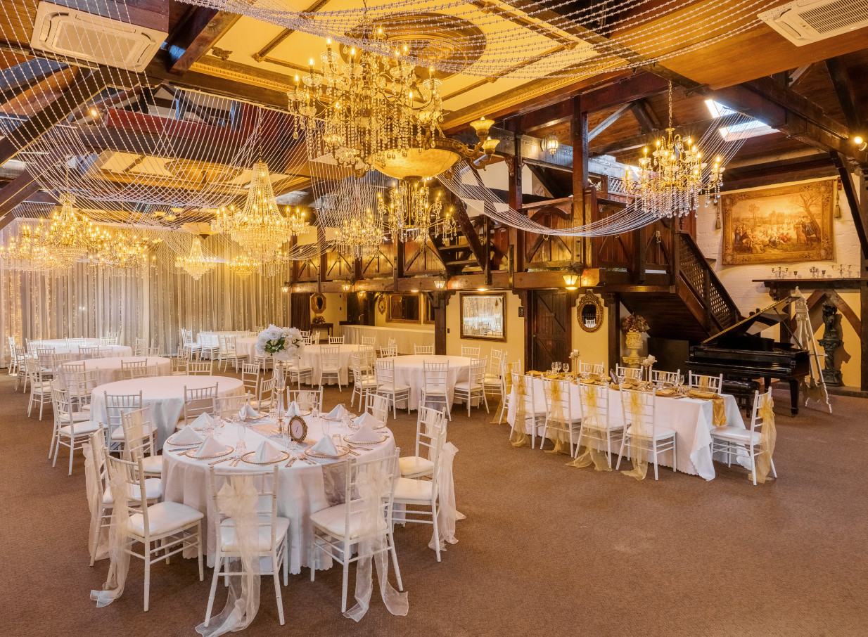 A grand, heritage-style reception hall at Settlers Country Manor in Auckland, adorned with sparkling chandeliers and wooden beams, set for an elegant event.