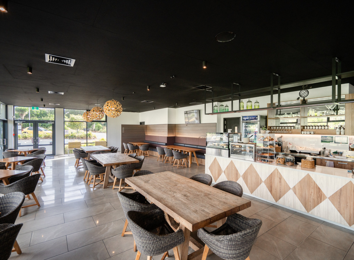 Wainui, Auckland's modern cafe and dining area, features warm wooden tables, woven chairs, and spherical pendant lighting.