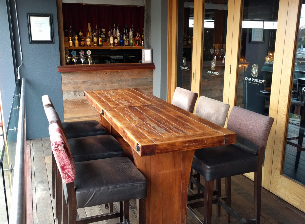 A South American-inspired outdoor bar seating area at Casa Publica, Christchurch, features a rustic wooden high-top table and stools.