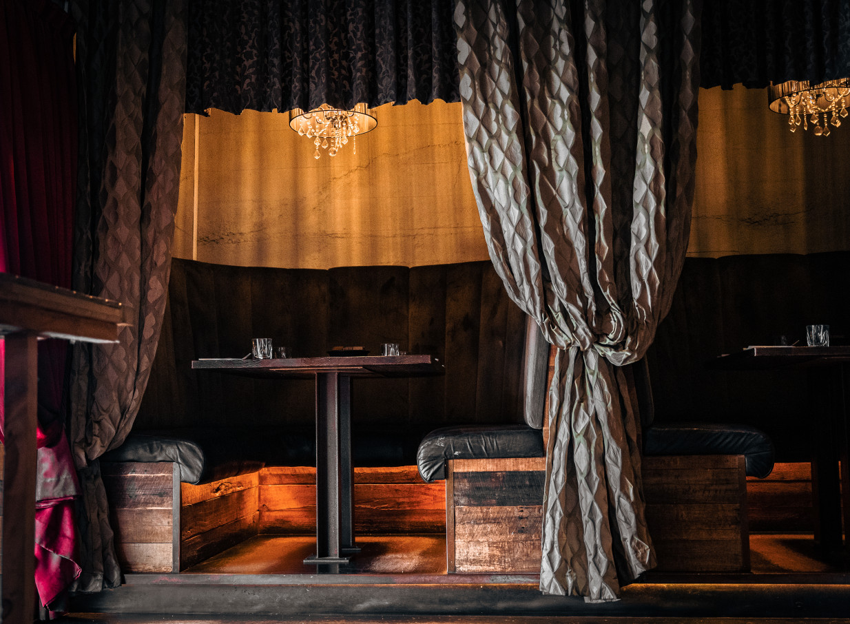 A private dining booth with dark wood and velvet curtains, showcasing Casa Publica's South American-inspired prohibition-era design in Christchurch.