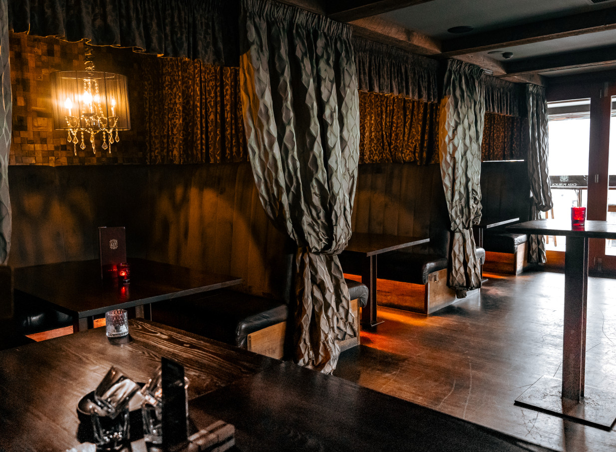 This alt text describes the moody, South American-inspired private dining booths with opulent curtains and a chandelier at Casa Publica in Christchurch.