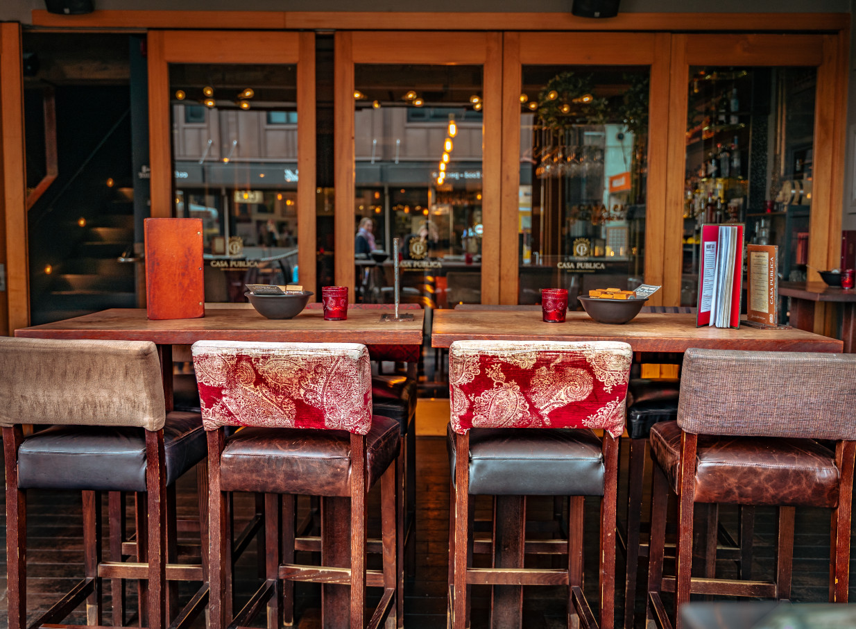 A vibrant outdoor dining area at Casa Publica in Christchurch, offering South American-inspired wooden tables and embroidered bar stools.