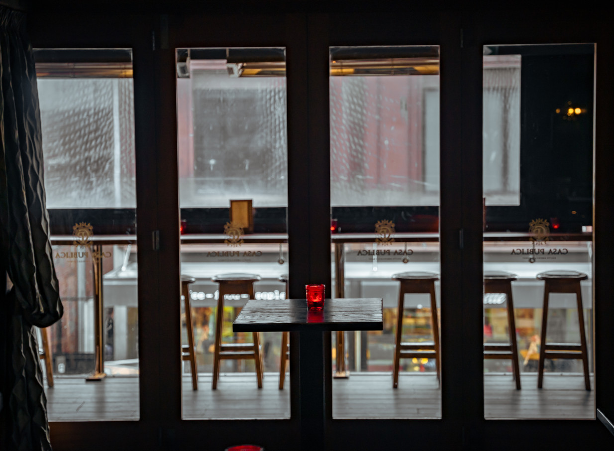 A moody, South American-inspired bar with tall windows and bar stools at Casa Publica, Christchurch.