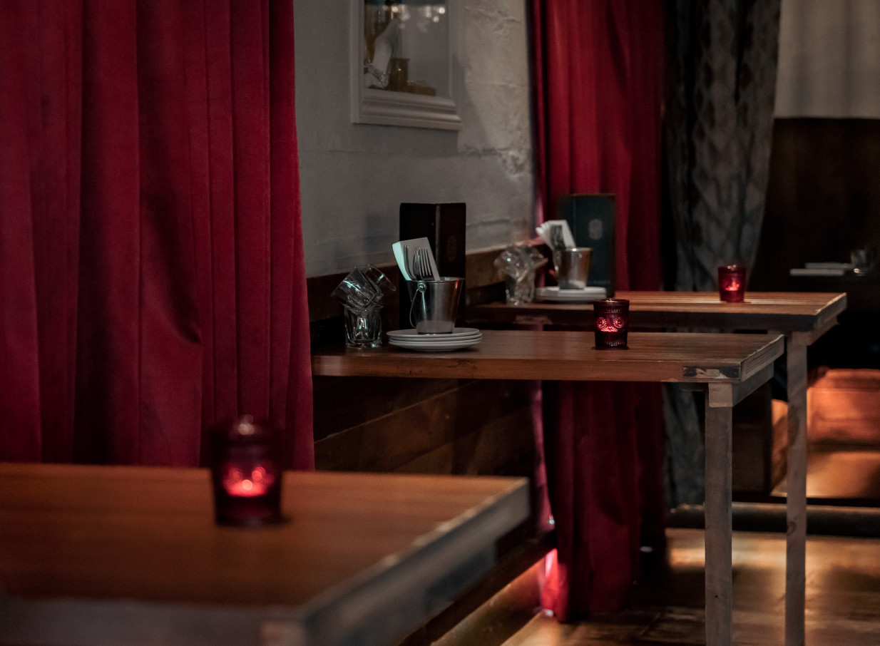 An intimate, South American-inspired dining area with red velvet curtains and set wooden tables at Casa Publica in Christchurch.