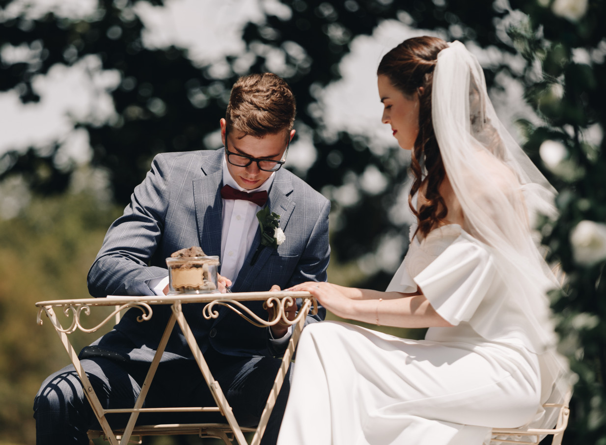 A couple signs documents at an outdoor ceremony in the manicured gardens of the historic Caccia Birch House, Manawatū-Whanganui.