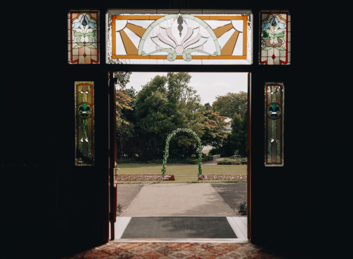 Caccia Birch House, a heritage homestead, hosts an outdoor ceremony viewed through its elegant stained glass doorway.