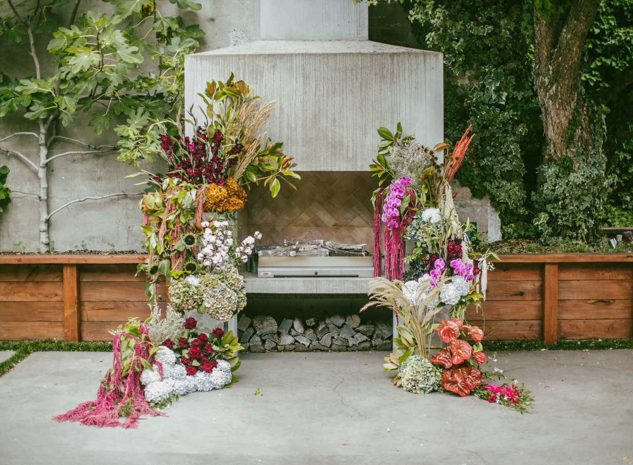 The French Cafe's elegant, French-inspired outdoor ceremony space in Auckland features a fireplace adorned with vibrant floral arrangements.