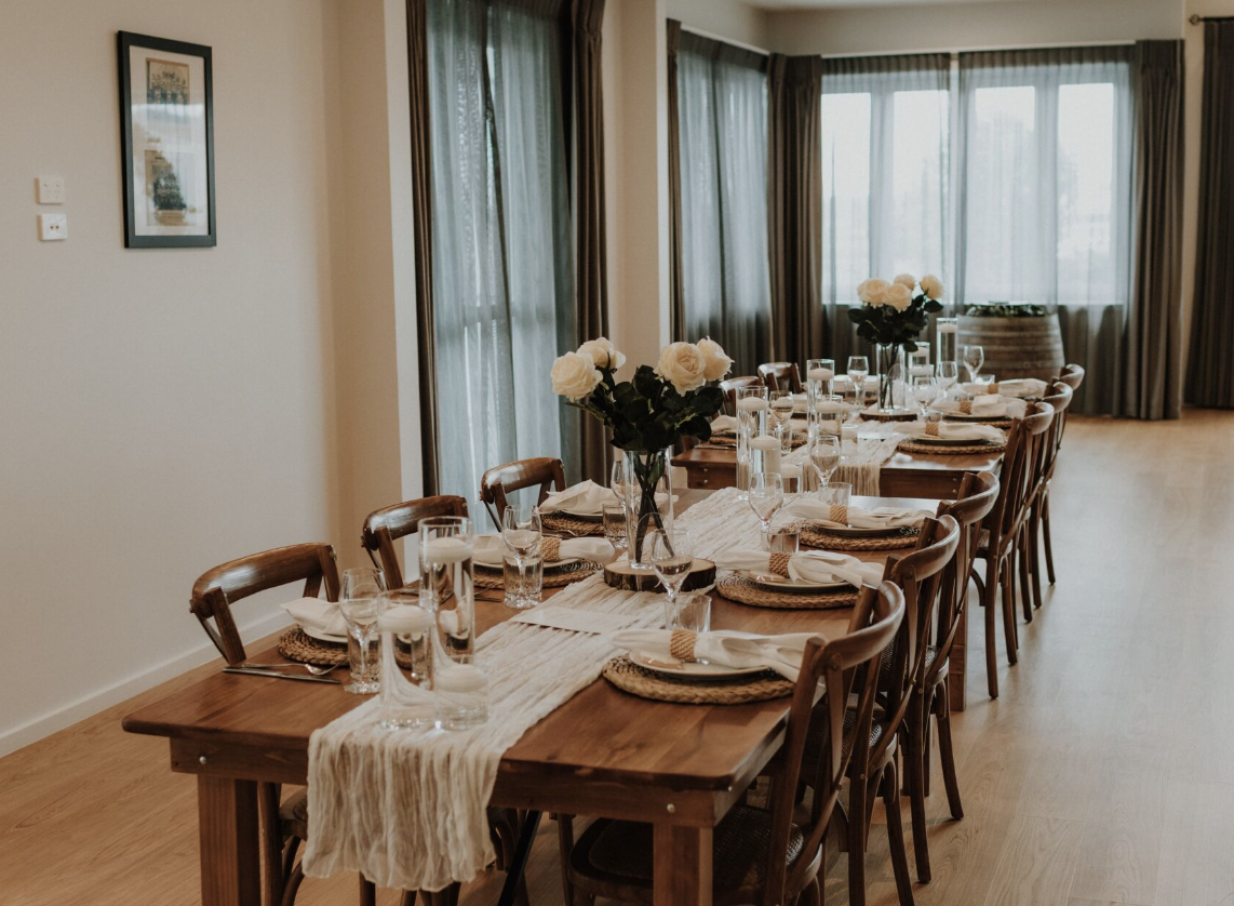 An elegantly set dining room at Tatum Park in Manawatū-Whanganui, featuring rustic wooden tables and white rose centerpieces.