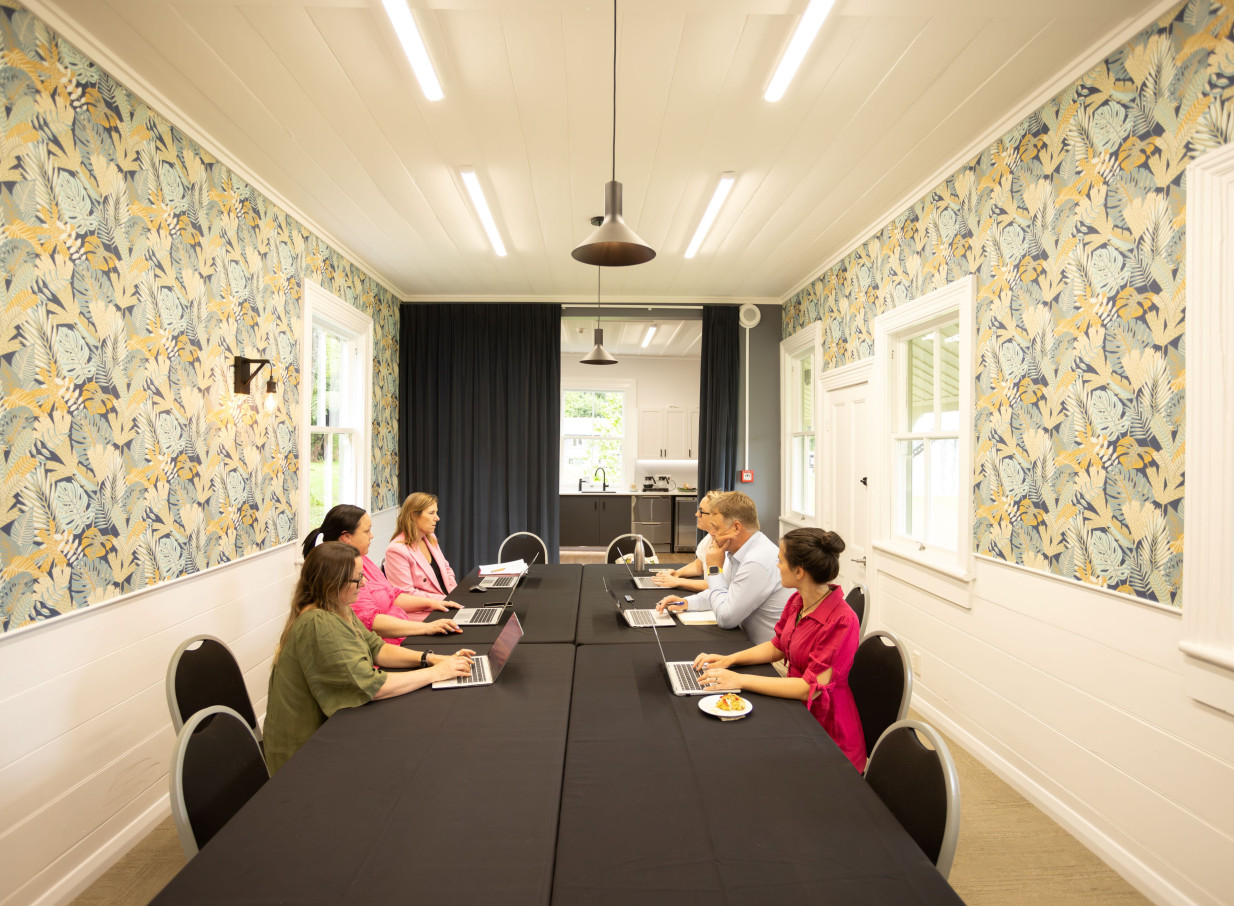 A meeting takes place in a heritage room at The Historic Village, Tauranga, featuring patterned wallpaper and modern amenities.