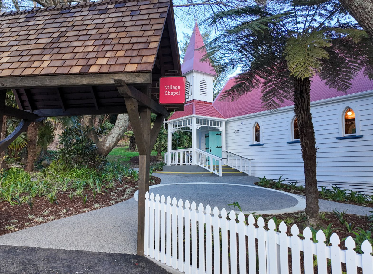 The charming, historic Village Chapel wedding venue at The Historic Village, Tauranga, with its distinctive red roof and picket fence.
