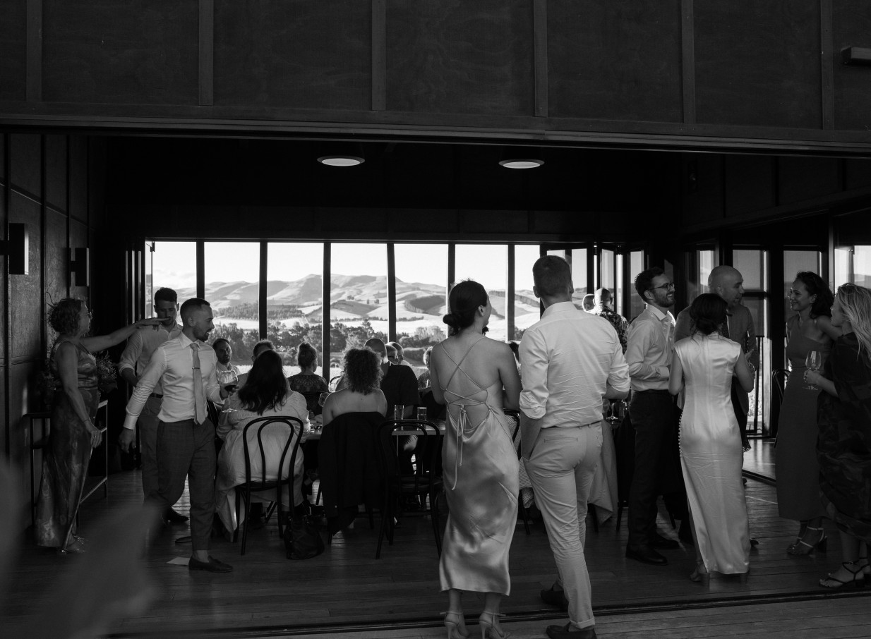 Guests mingle in the modern, architect-designed event space at Black Estate Winery, Christchurch, with panoramic vineyard views.