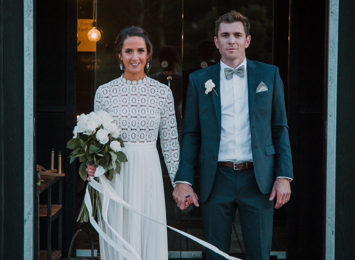 A wedding couple stands within the dark-stained timber interior of Black Estate Winery in Christchurch, known for its rural-inspired architecture.