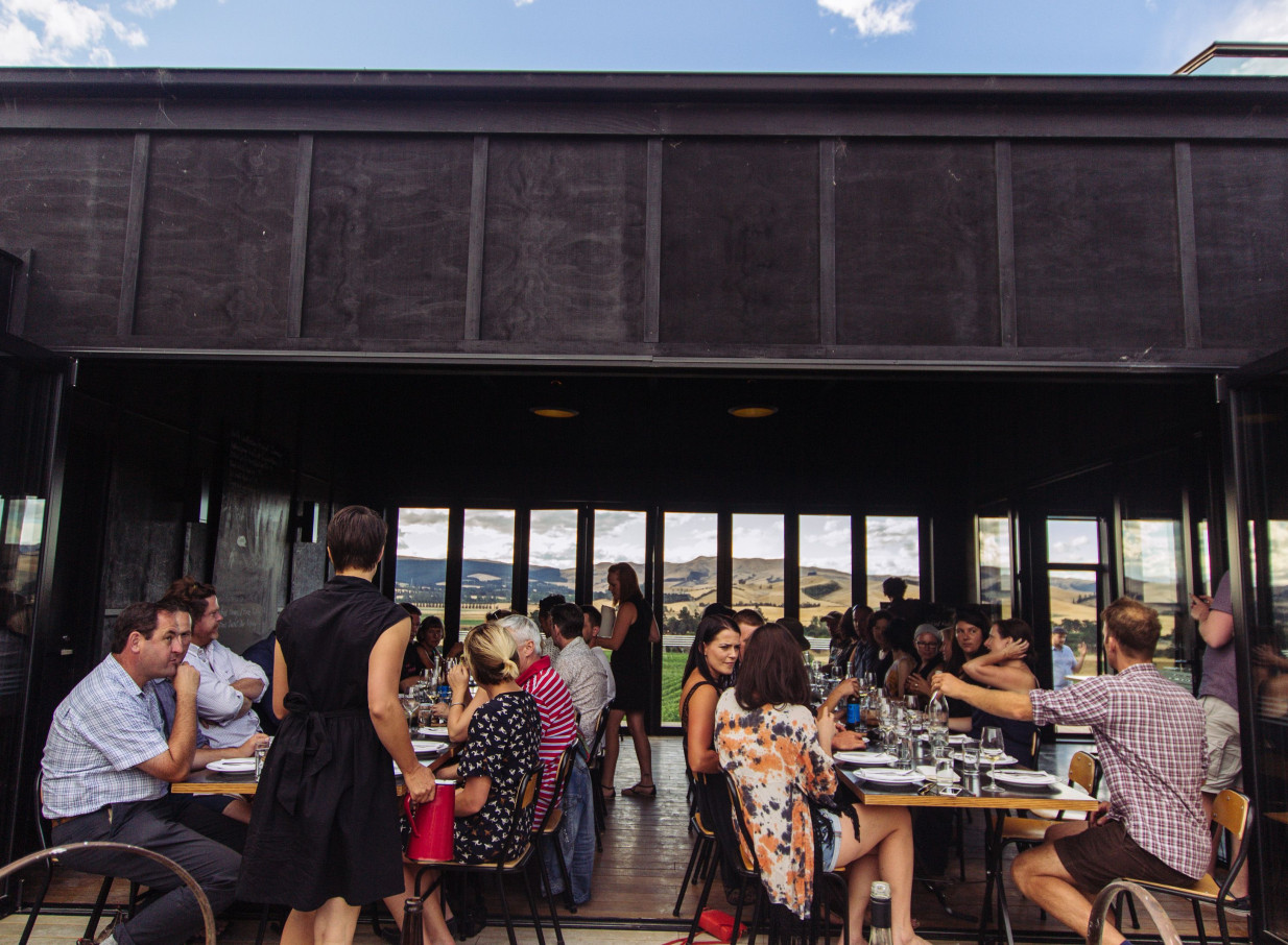 Guests dine in the modern, dark-stained timber restaurant at Black Estate Winery in Waipara Valley, enjoying vineyard views.