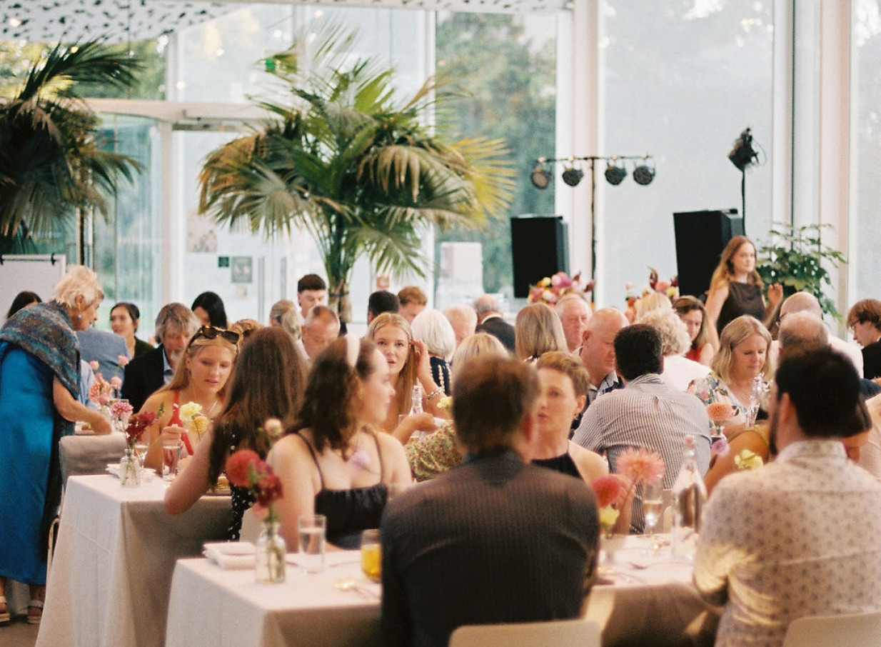 A dining event at ilex Christchurch's contemporary venue, featuring floor-to-ceiling windows and lush indoor palm trees.