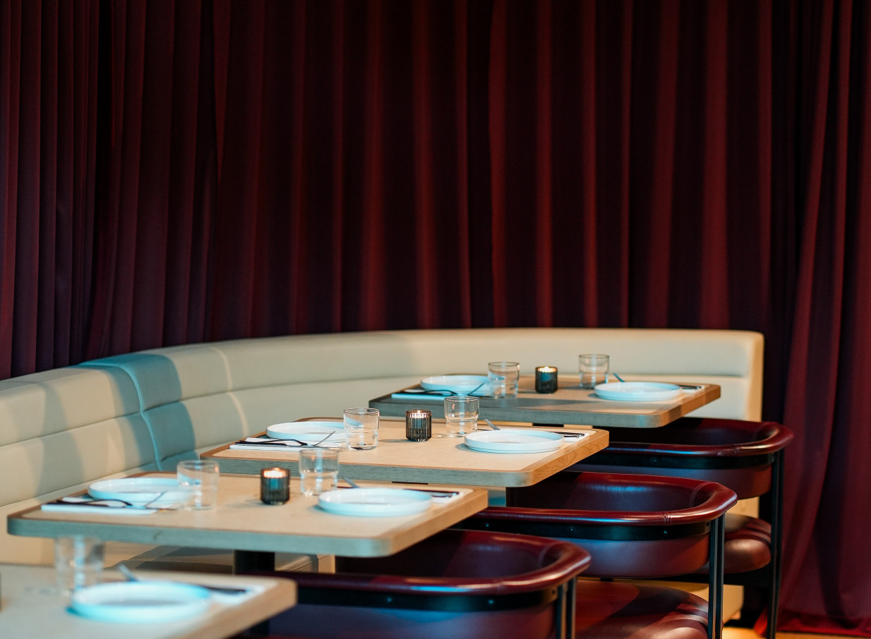 A chic dining area at Darling on Drake in Auckland, featuring cream booth seating, set tables, and dramatic red curtains.