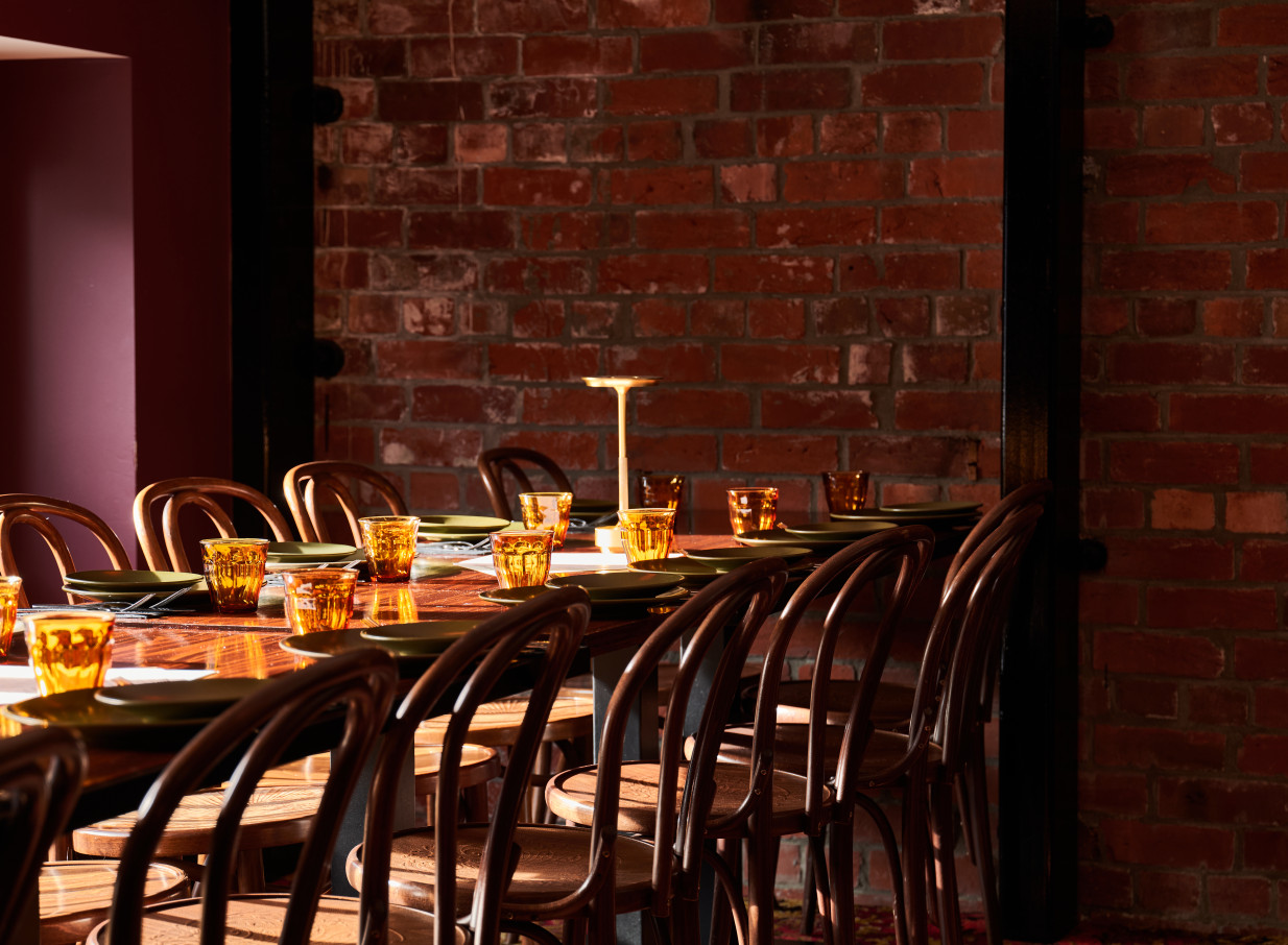 An intimate dining room at The Monday Room in Christchurch, featuring a historic brick wall and warm wooden chairs.